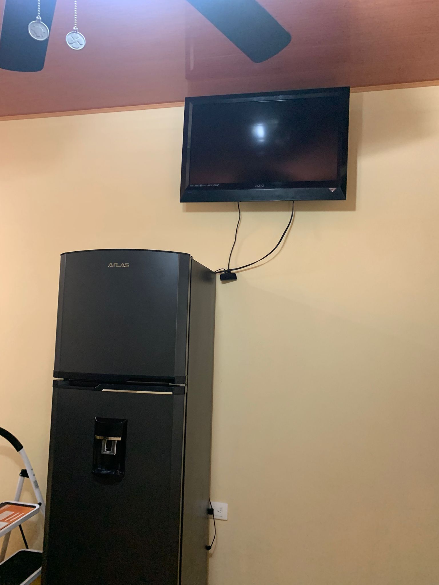 A black refrigerator with a control panel and a flat-screen TV mounted on the wall.