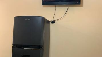 A black refrigerator with a control panel and a flat-screen TV mounted on the wall.