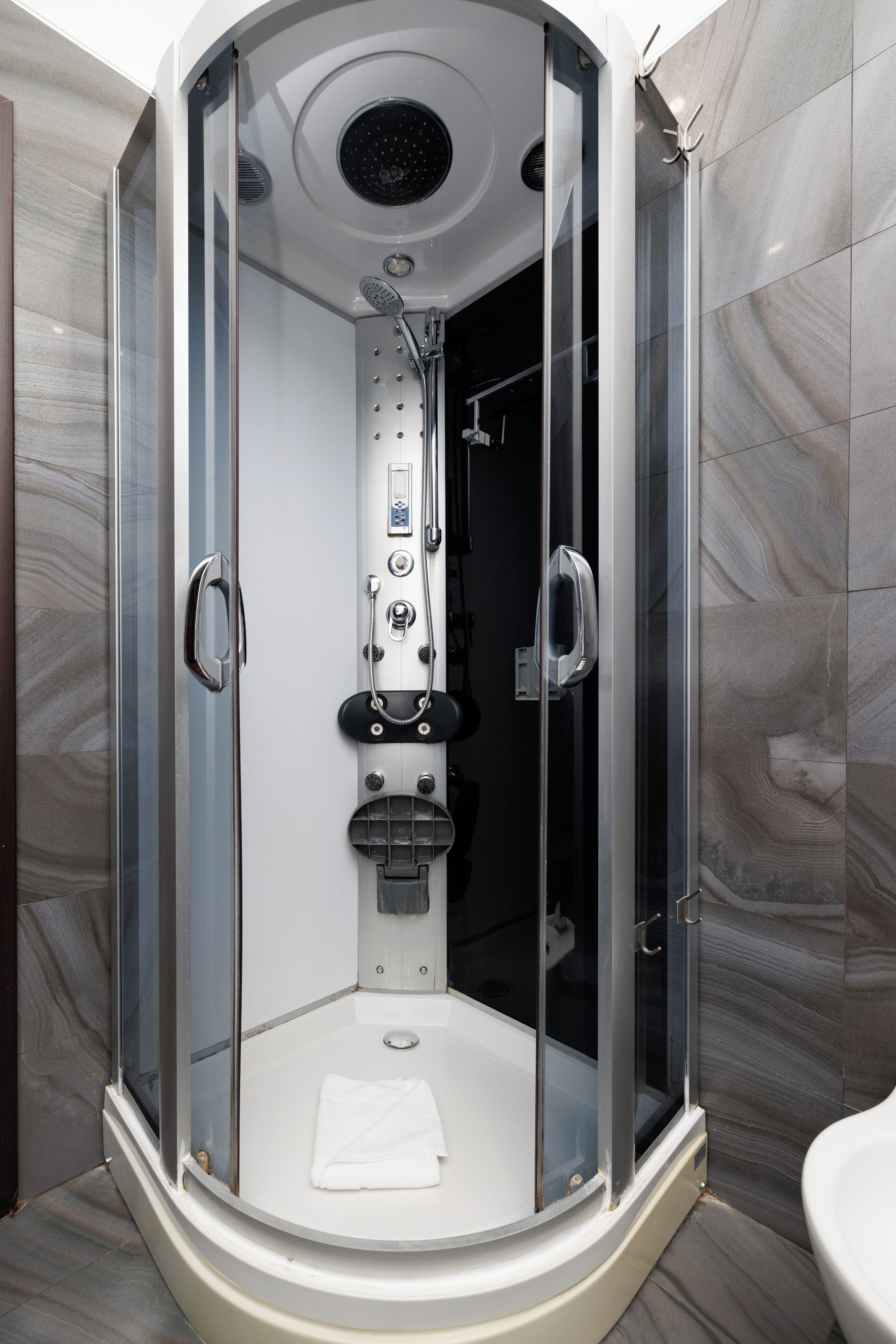 Una cabina de bany moderna i tancada amb porta de vidre, un panell de control i una tovallola blanca al terra.