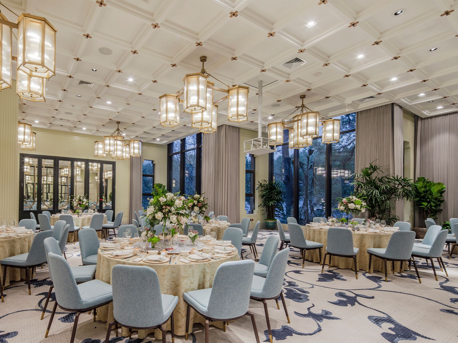 A banquet hall with round tables, light blue chairs, and chandeliers.