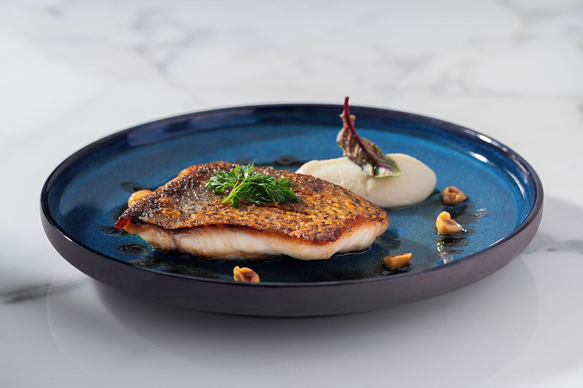 Une assiette avec un morceau de poisson, une cuillère de crème et quelques noix.