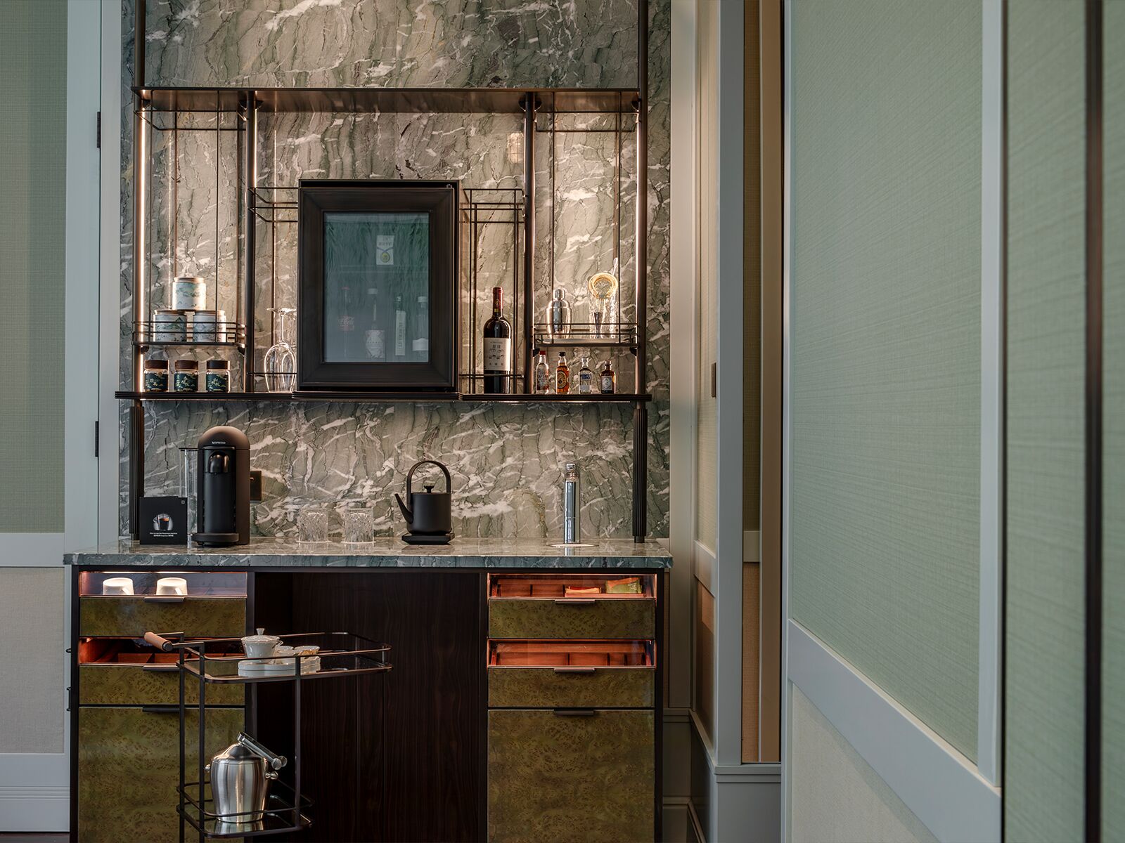 A modern kitchen with marble countertops, a built-in coffee machine, a kettle, and a wine rack.