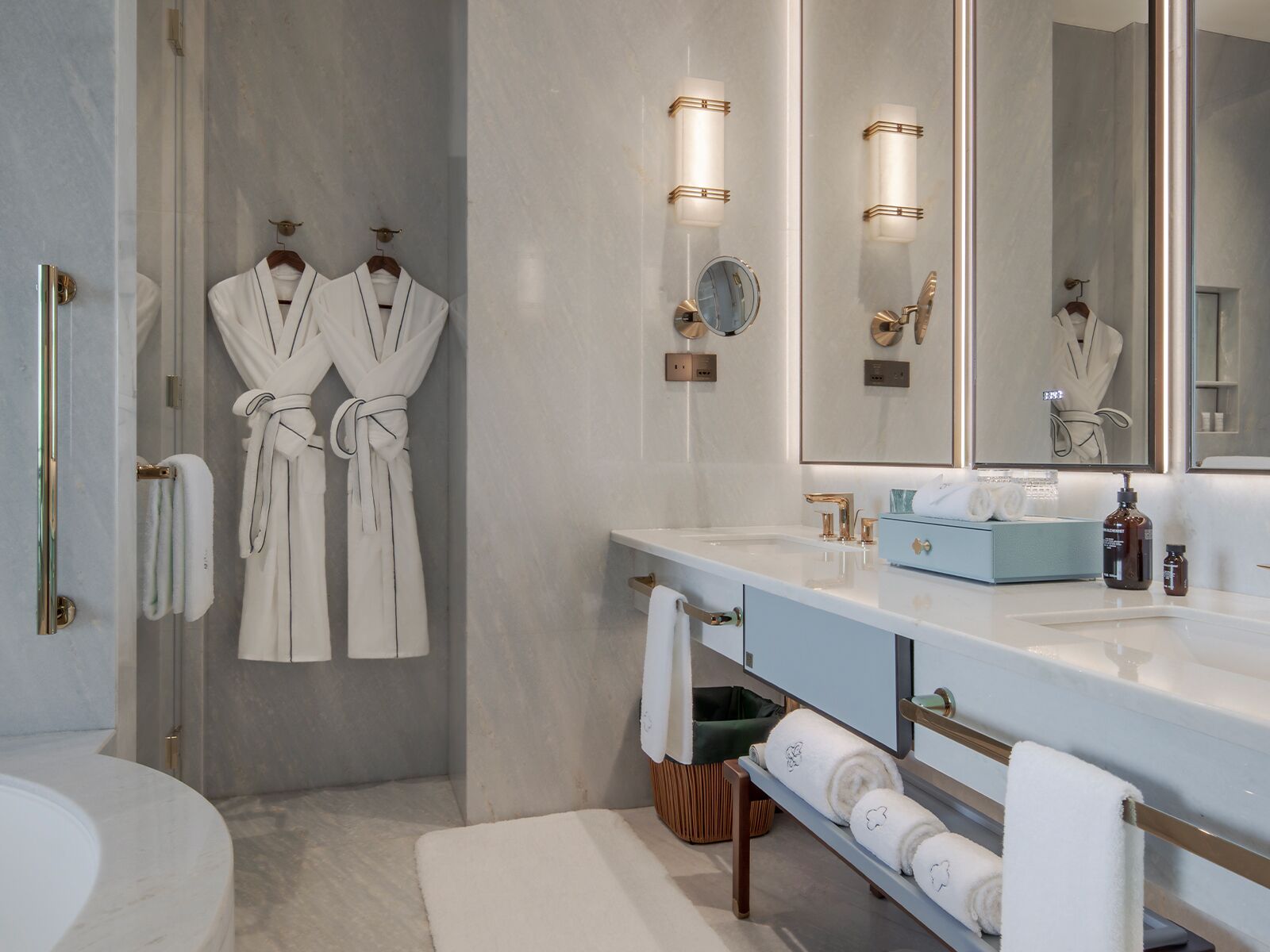 Un baño moderno con un espejo grande, dos batas colgadas en ganchos, un tocador con encimera azul y una bañera.