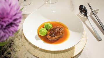 A white plate with a piece of meat, green garnish, and sauce.