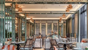 Ein Restaurant mit hohen Decken, grünen Metallgeländern und einer zentralen Bar. Tische und Stühle sind zum Essen bereitgestellt.