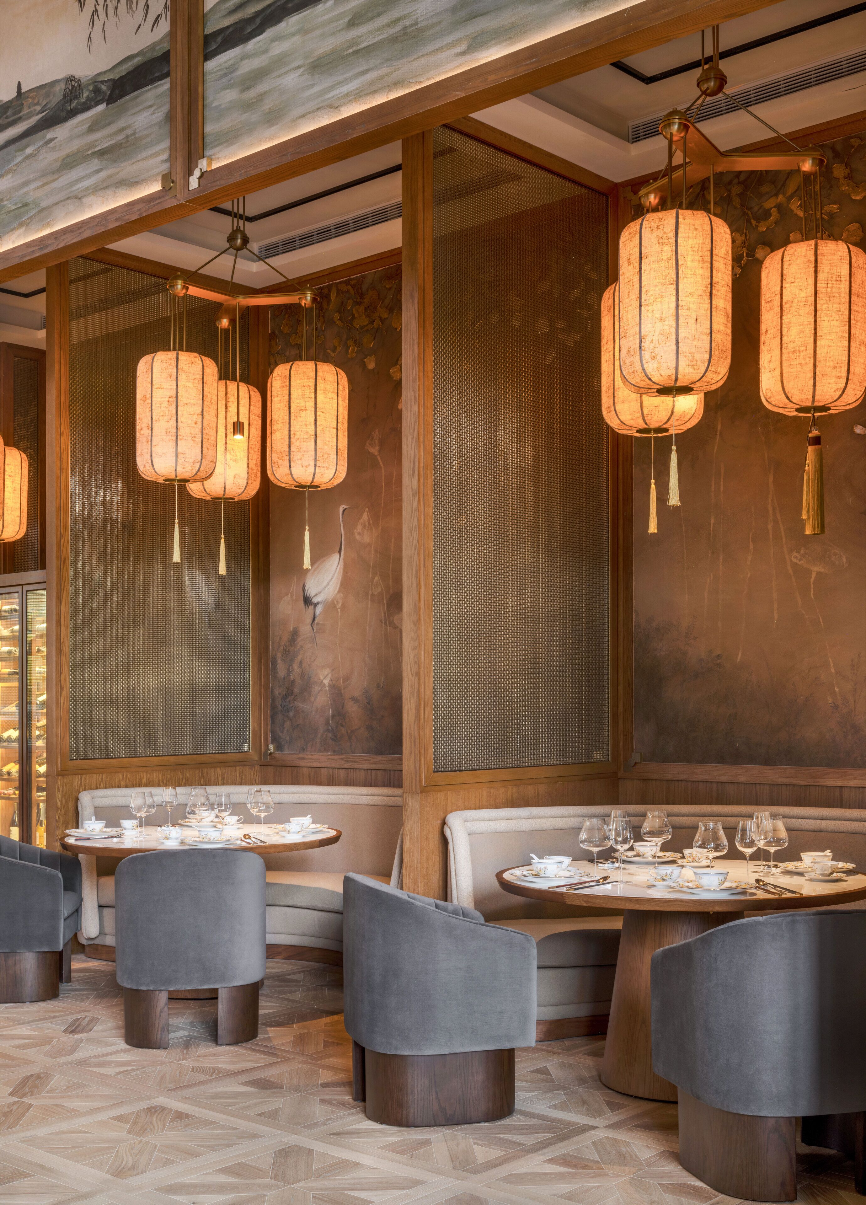 A restaurant interior with round tables, grey upholstered chairs, and traditional lantern-style lighting.