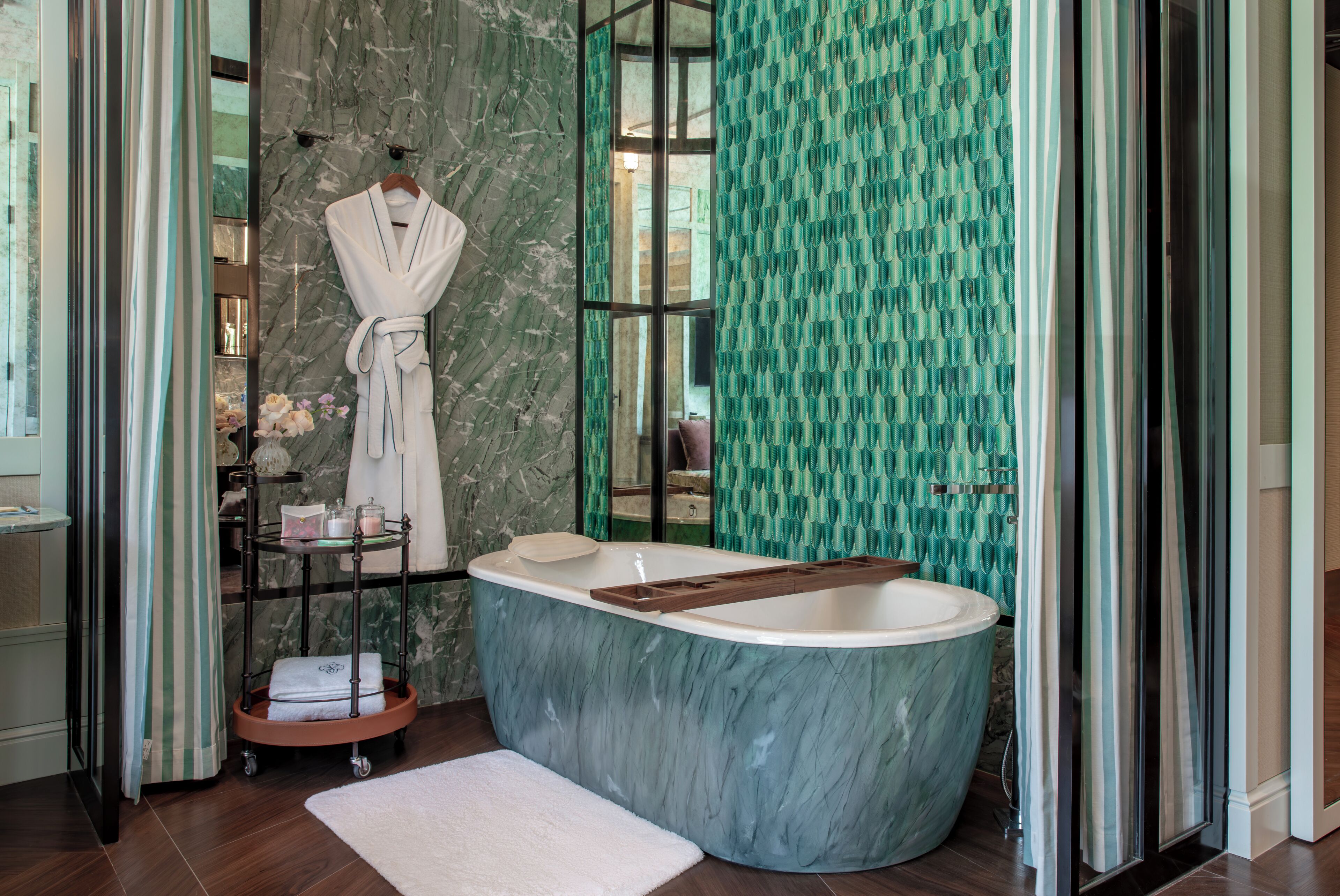 A bathroom with a marble bathtub, a robe hanging on a rack, and a shower with a green patterned curtain.