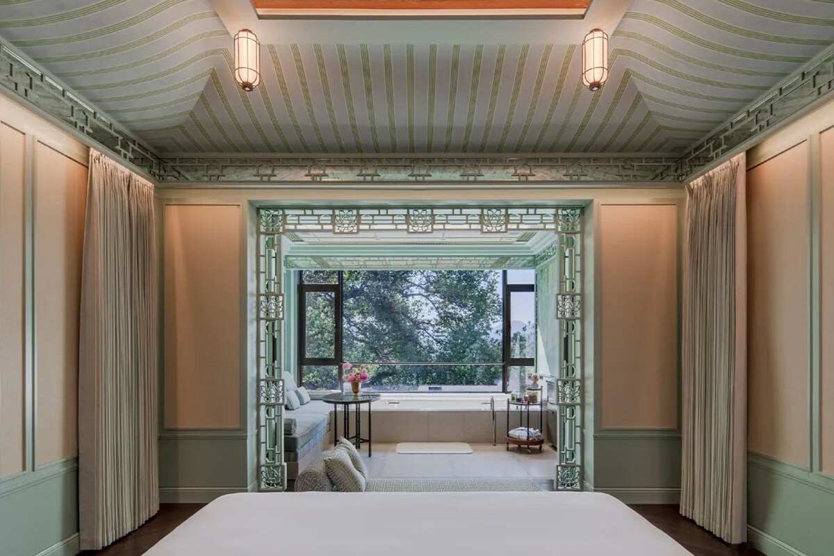 Quarto com cama grande, janela com vista para árvores e teto decorativo.