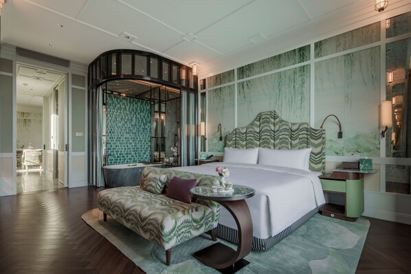 A modern hotel room with a large bed, a curved seating area, a round table, and a unique curved wall feature.