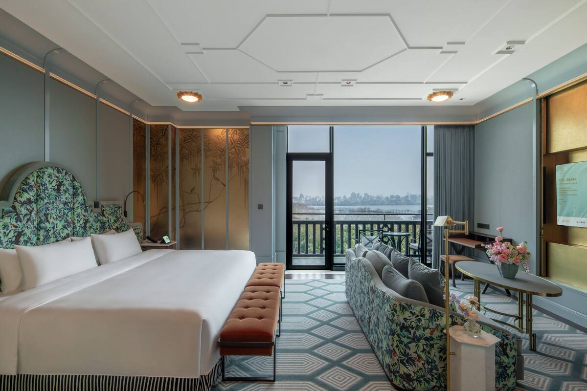 A hotel room with a large bed, a sofa, a small table, and a view of the city.