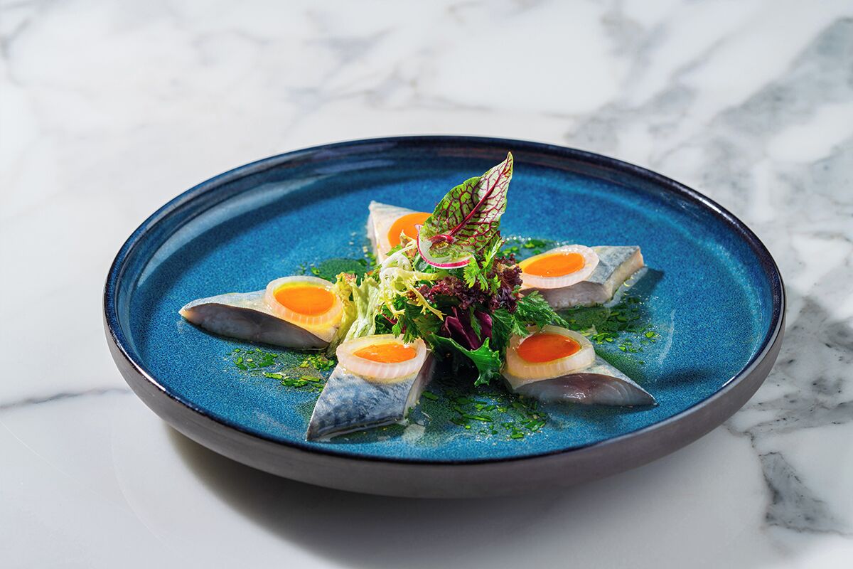 A blue plate with a seafood dish, including fish and egg garnishes, on a marble surface.