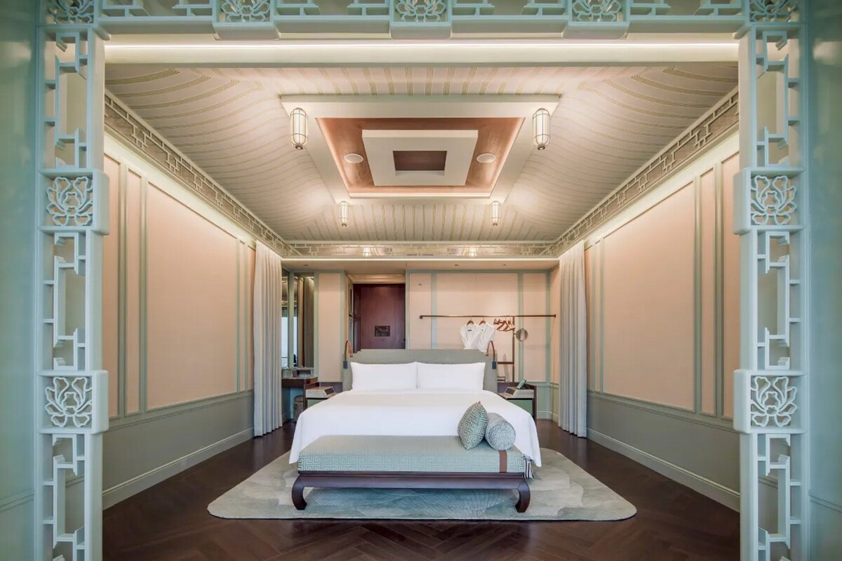A spacious bedroom with a large bed, a decorative ceiling, and a nightstand with a lamp.