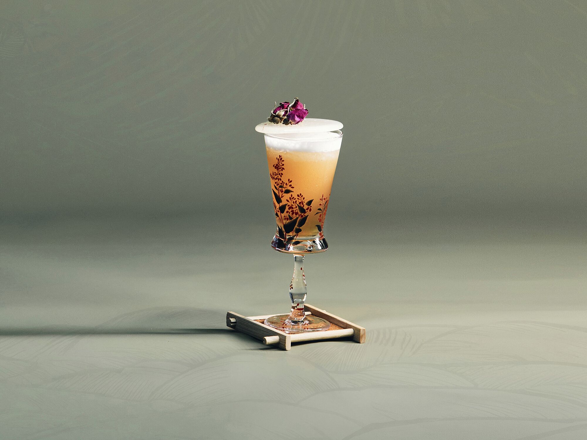 A tall glass with a floral design, filled with a light-colored beverage, placed on a coaster.