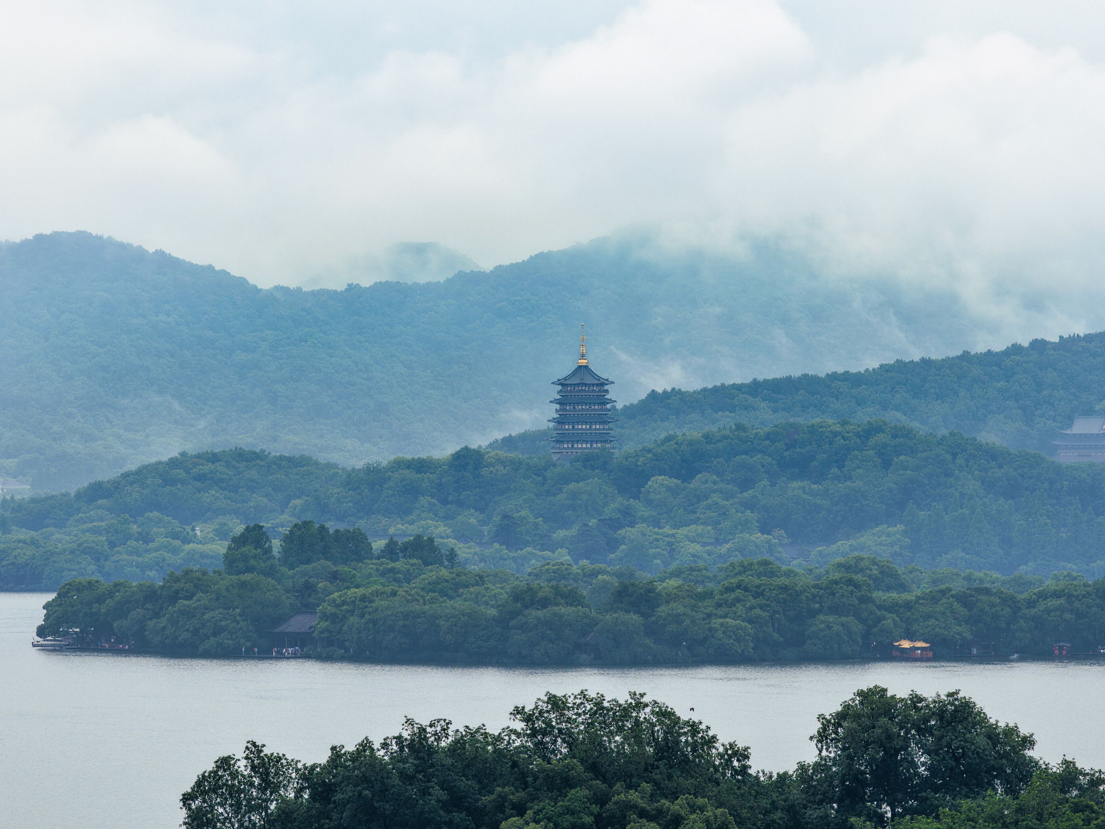 Um pagode numa colina com vista para um lago, rodeado por uma floresta densa.