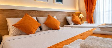 Habitación de hotel con dos camas, ropa de cama naranja, almohadas blancas y una obra de arte en la pared.