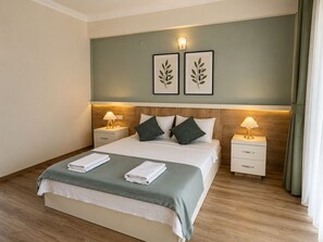 Habitación de hotel con cama, dos mesitas de noche, lámpara de pared y planta en un marco colgado en la pared.