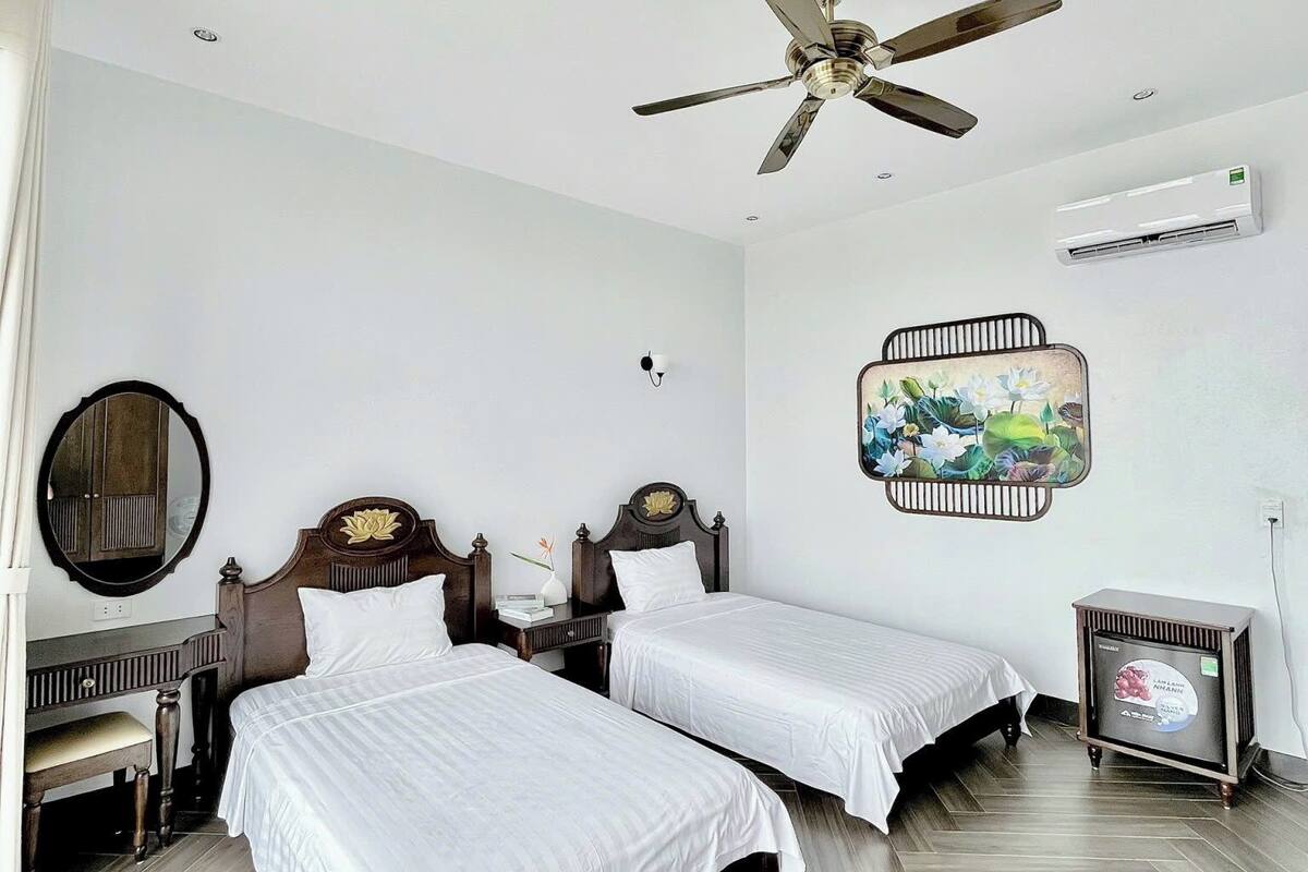 Hotelkamer met twee bedden, een plafondventilator, airconditioning, een spiegel aan de muur en een decoratief kunstwerk.