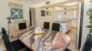 A dining area with a marble table, black chairs, a wooden cabinet, and a kitchen in the background.