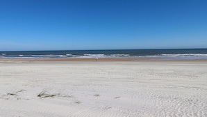 A wide sandy beach with a clear blue sky and ocean in the background.
