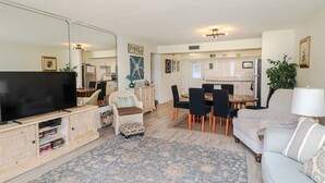 A living room with a television, a dining table with chairs, a sofa, and a large rug.