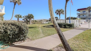 A residential area with a clear sky, palm trees, a gated entrance, and a building with balconies.