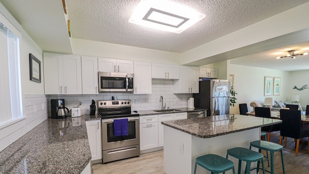 A modern kitchen with white cabinets, a granite countertop, stainless steel appliances, and a central island with bar stools.