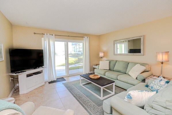 A living room with a flat-screen TV, a sofa, a coffee table, and a sliding glass door leading to a balcony.