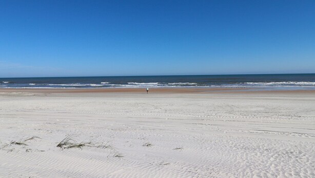 Une vaste plage de sable fin, avec des vagues douces et un ciel bleu limpide.