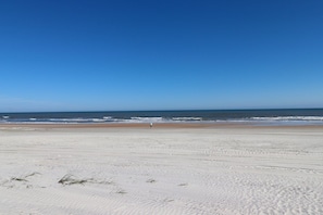 A wide sandy beach with gentle waves and a clear blue sky.