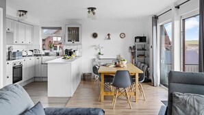 Una cocina moderna con armarios blancos, una isla central y un comedor con mesa y sillas de madera.