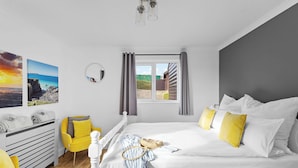 Un dormitorio con cama, una silla, un aparador y una ventana con cortinas.