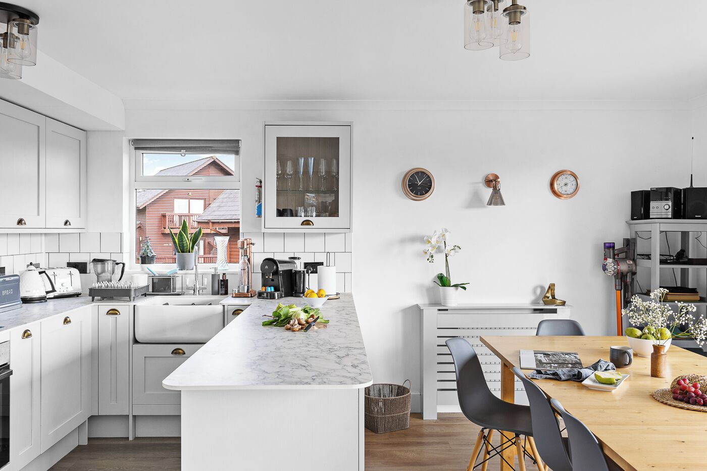 A modern kitchen with white cabinetry, a marble island, and a dining area with a wooden table and chairs.