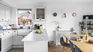 Una cocina moderna con muebles blancos, una isla de mármol y un comedor con mesa y sillas de madera.