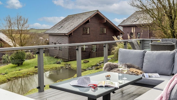 Un balcón con una mesa de vidrio, un sofá y vistas a casas de madera a través de un río.