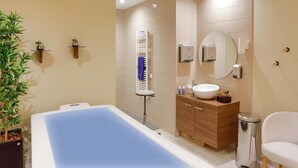 A modern bathroom with a bathtub, a sink, a mirror, and a toilet. There are two potted plants on the left side. - Domitys Le fil de soie  (Calais)