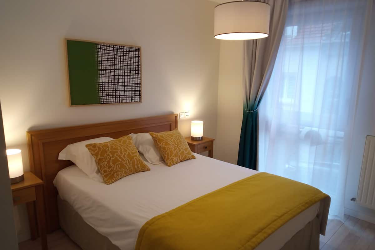 Ein ordentlich bezogenes Bett mit weißer und gelber Bettwäsche, ein Holz-Kopfteil und zwei Nachttischlampen.