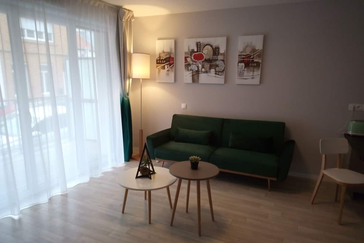 Ein Wohnzimmer mit einem grünen Sofa, zwei runden Tischen, einer Stehlampe und drei Wandbildern.