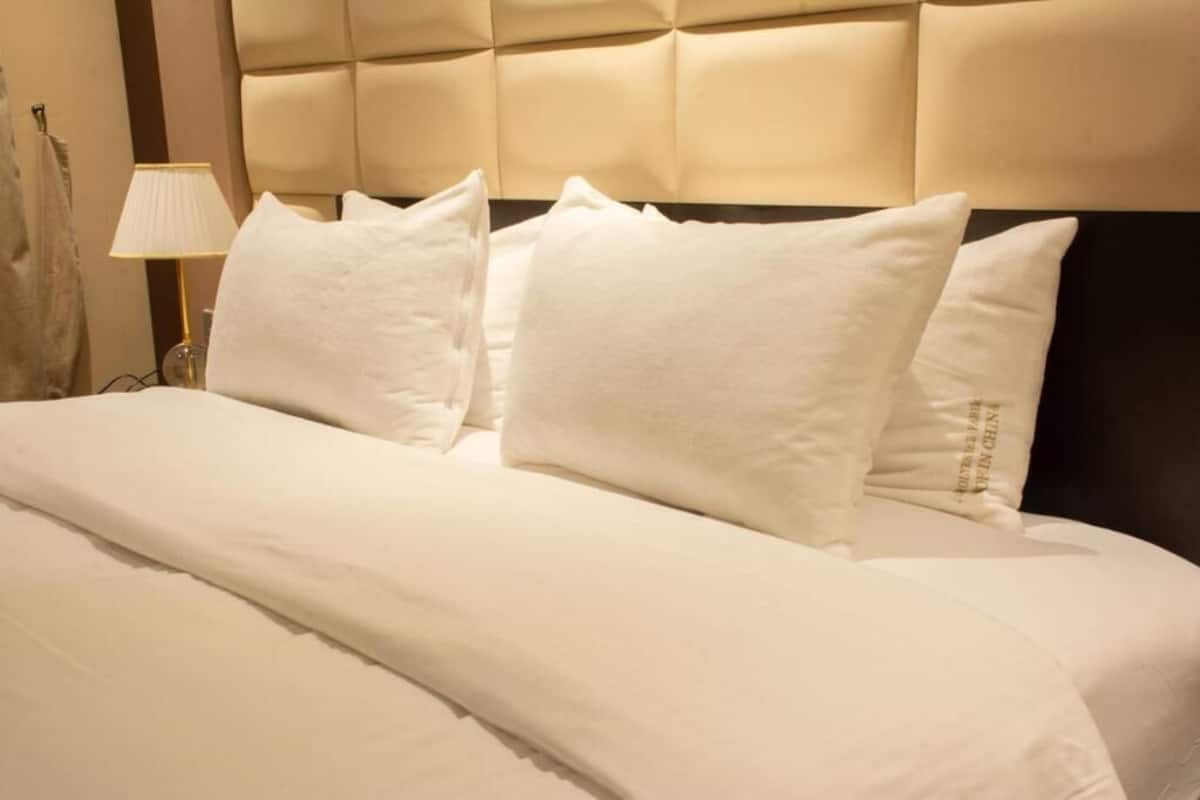 A neatly made bed with white linens and pillows, a tufted headboard, and a bedside lamp.