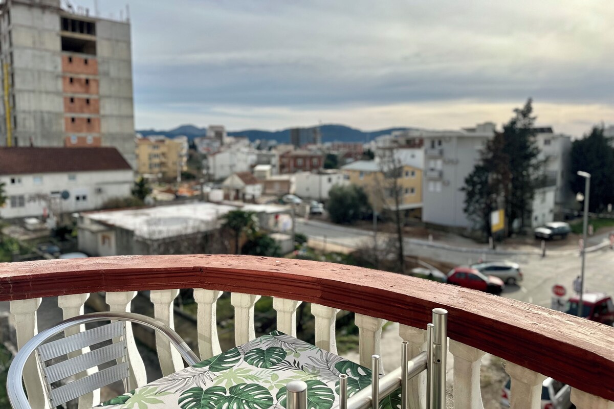A balcony with a view of a cityscape, including buildings and mountains.