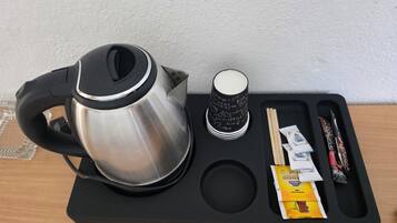 A black tray with a stainless steel kettle, a cup with black text, chopsticks, a pen, and a packet of snacks.