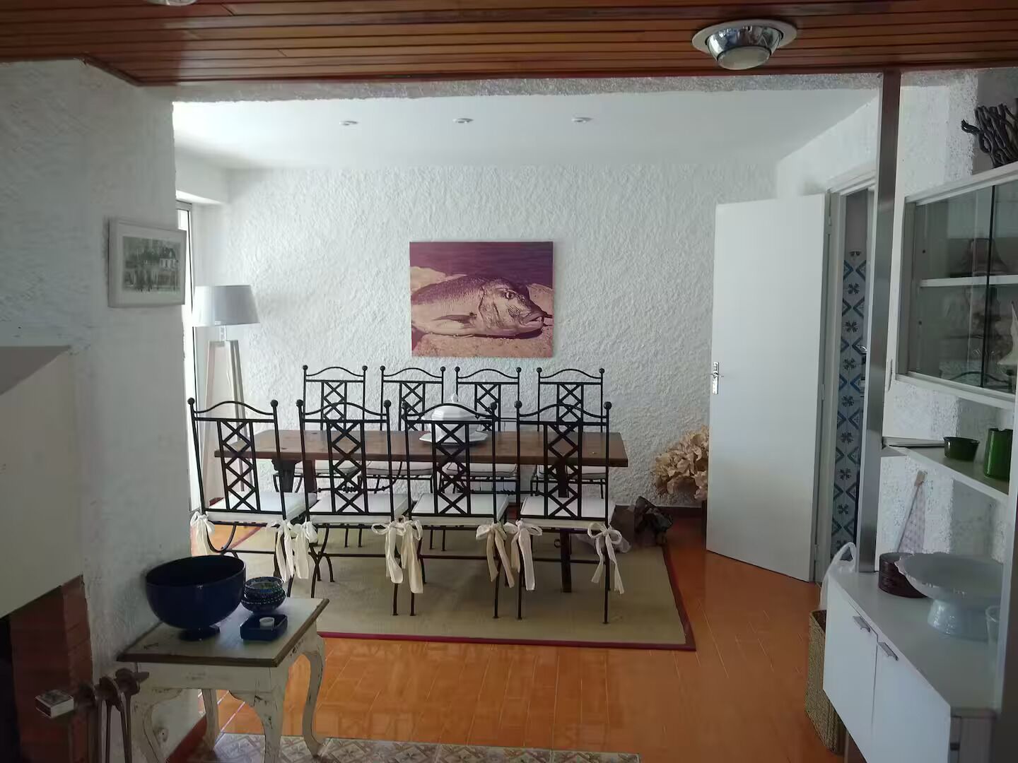 Un coin repas avec une table et des chaises en bois, un tableau au mur et un espace cuisine avec des placards et un évier.