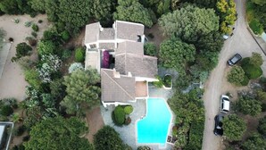 Vista aérea de una casa con piscina, rodeada de abundante vegetación y un camino de entrada con coches estacionados.
