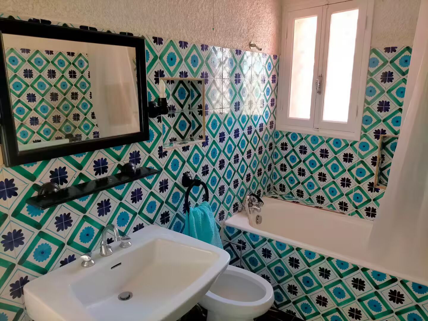 A bathroom with a sink, toilet, and bathtub. The walls are tiled with a geometric pattern.