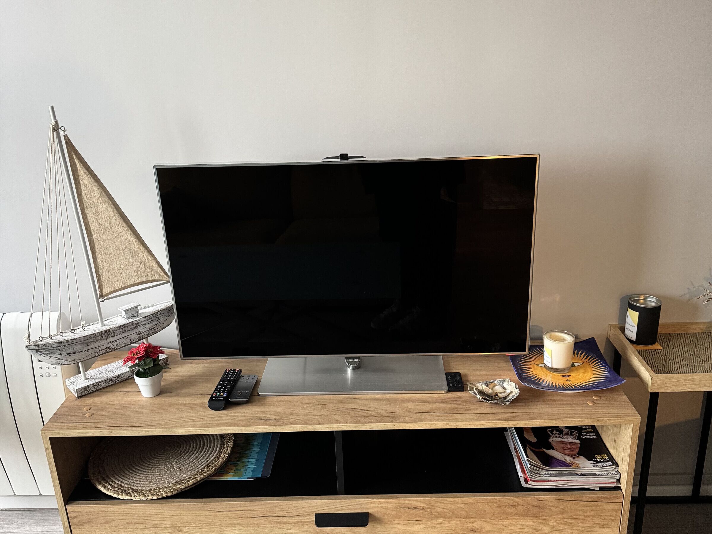 Un mueble de televisión de madera con un televisor de pantalla plana, un modelo de velero, un control remoto, una vela y una revista.