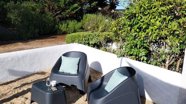 Dos sillones reclinables negros con cojines azul claro, una mesita con un vaso y una jardinera blanca.