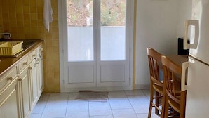 A kitchen with yellow tiles, a white door, a wooden chair, and a wine-themed wall decoration. - Sunny F2 near spa, pets allowed (Amélie-les-Bains-Palalda)