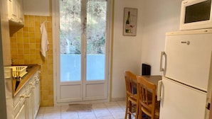 A compact kitchen with a double door leading to a balcony, a dining table with chairs, and a refrigerator. - Sunny F2 near spa, pets allowed (Amélie-les-Bains-Palalda)