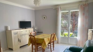 A dining area with a table and chairs, a television on a cabinet, and a green sofa. - Sunny F2 near spa, pets allowed (Amélie-les-Bains-Palalda)