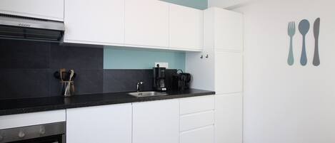 A modern kitchen with white cabinets, a black countertop, a coffee maker, and a sink.