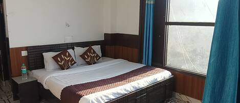 A neatly made bed with a white and brown bedspread, two decorative pillows, a water bottle on a nightstand, and a window with blue curtains.